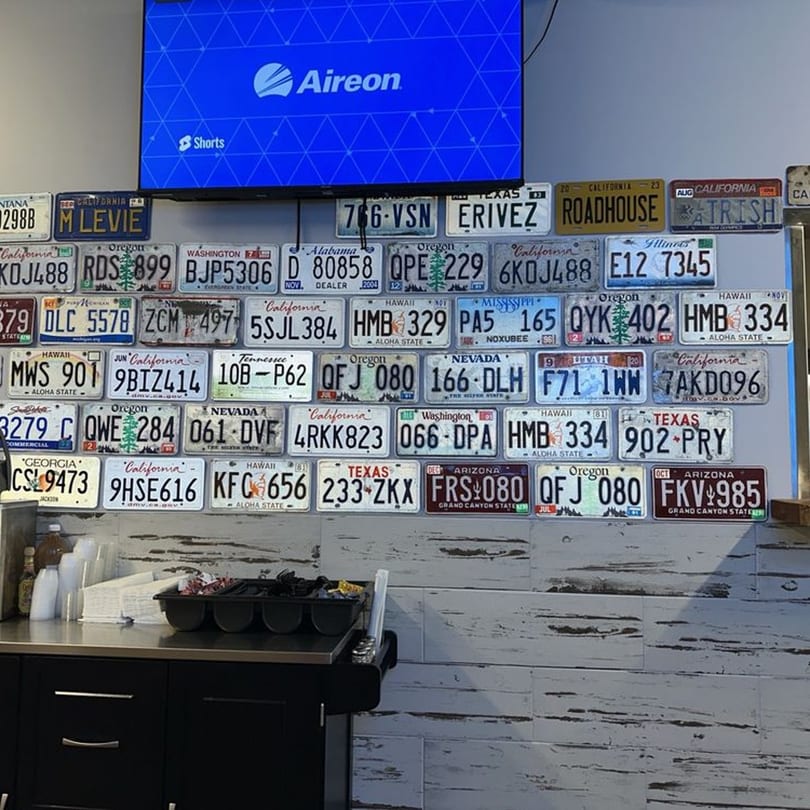 A wall decorated with numerous colorful license plates from various states above a dark counter.
