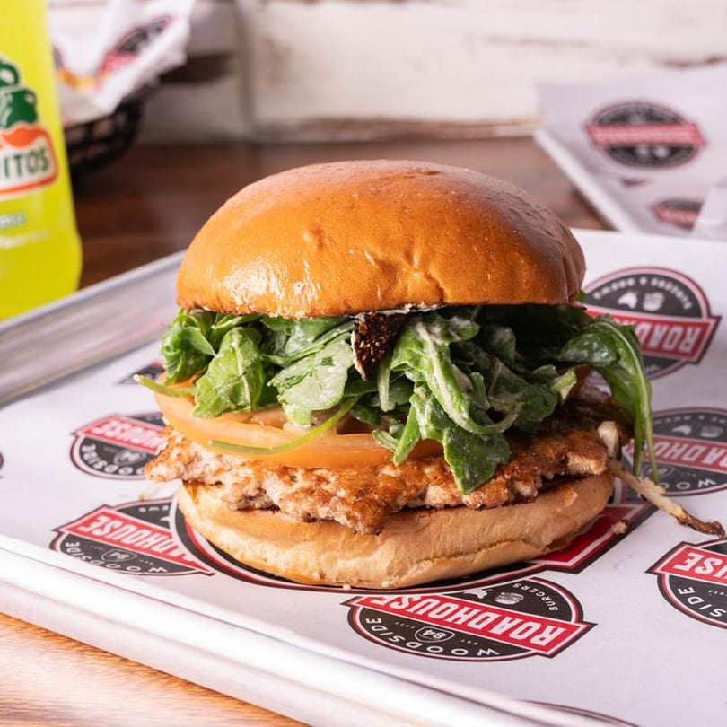 Woodside Roadhouse burger with a golden bun, patty, tomato, and arugula on branded paper.