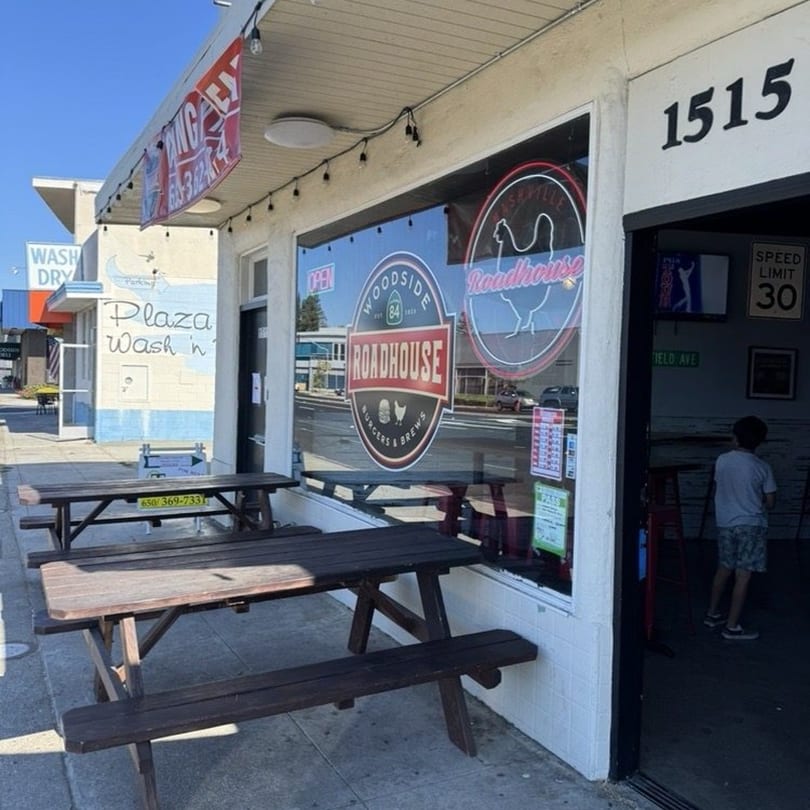 Exterior of Woodside Roadhouse with picnic tables outside and a child standing in the doorway.